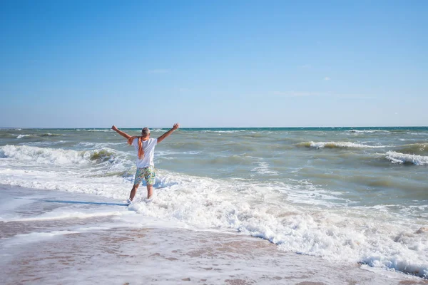 Happy man stands on the beach in surf line, with outstretched ar
