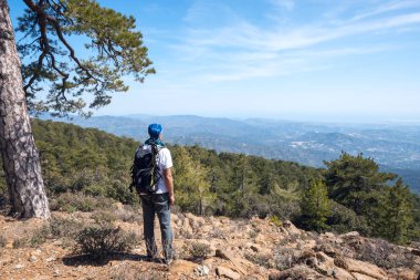 Traveler with backpack stands on a rocky slope clipart