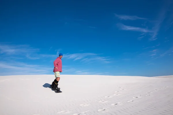Uśmiecha się człowiek slajdy w dół na snowboardzie na piaszczystych wydmach — Zdjęcie stockowe