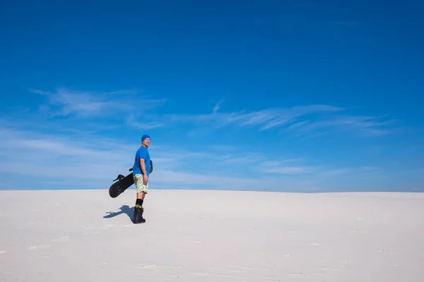 Mutlu bir adam elinde bir snowboard ile kumul üzerinde duruyor — Stok fotoğraf