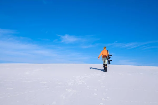 Chico con gorra divertida con una tabla de snowboard sube a la duna de arena — Foto de Stock