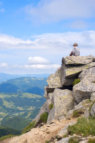 Kid in het GLB zittend op een rotsachtige top in de bergen — Stockfoto