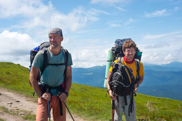 Homens sorridentes, viajantes com mochilas estão de pé na montanha — Fotografia de Stock