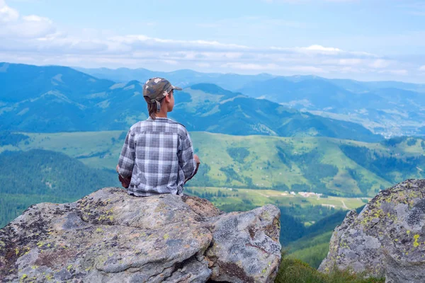 Jongen zit op de rots in de voorkant van de bergen — Stockfoto