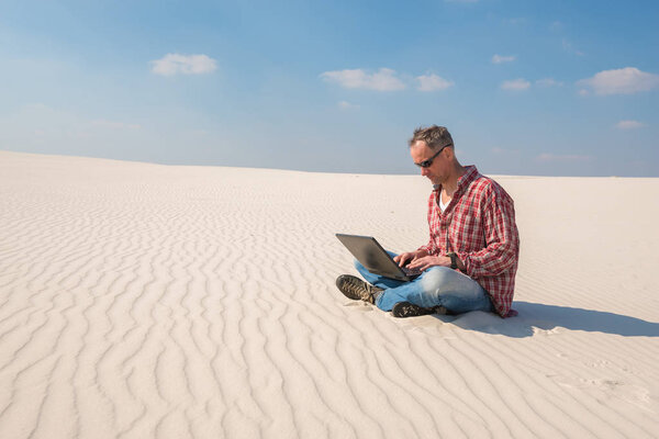 Обеспокоенный человек с ноутбуком сидит в пустыне
