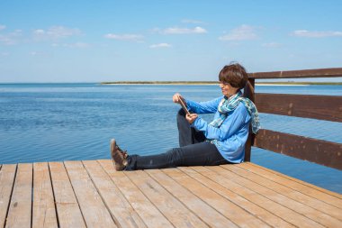 Rahatlatıcı kadın tablet ile ahşap bir iskele üzerinde oturuyor