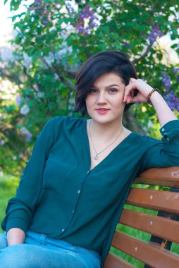 Modern çok ırklı bir blossomin altında bir Bank üzerinde rahatlatıcı bir kızdır