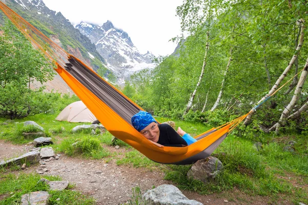 Счастливая забавная женщина путешественница отдыхает в гамаке в горах — стоковое фото