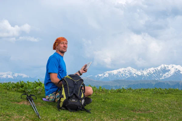 Gelukkig reiziger zit op de alpine weide met een tabletcomputer — Stockfoto