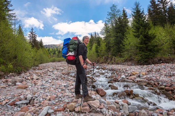 Homem viajante com mochila cruza um rio de montanha — Fotografia de Stock