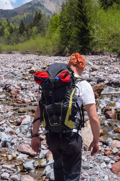 Aventureiro com mochila cruza um rio de montanha — Fotografia de Stock