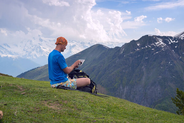 Man traveler sits on the mountain plateau next to clouds 