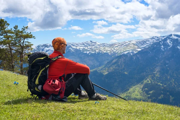 Человек авантюрист сидит на альпийском лугу среди полевых цветов — стоковое фото