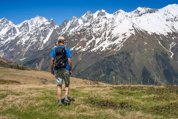 Человек турист идет вдоль альпийского луга к заснеженной горе р — стоковое фото