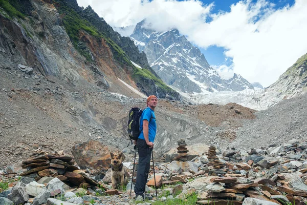 Человек-авантюрист с большой собакой стоит перед ледником — стоковое фото