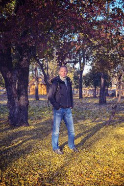 Adam renkli düşen yaprakları arasında bir parkta duruyor
