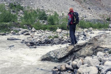 Gezgin, sırt çantası ile dağ nehir yanında duruyor