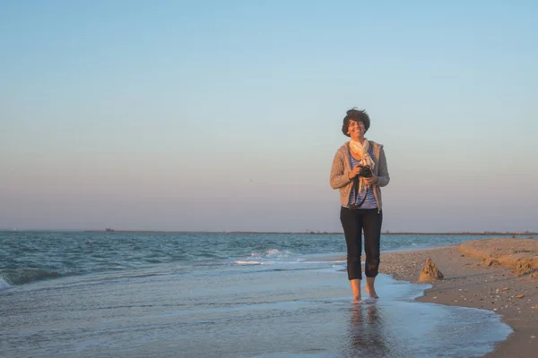 Mujer alegre está caminando por la playa con la cámara — Foto de Stock