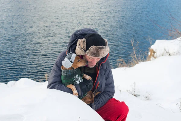 Gelukkig man knuffels kleine hond, dragen in een grappige winter hoed — Stockfoto