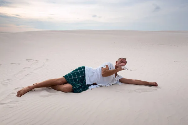 Wyczerpany mężczyzna leży na piasku i napoje pozostałości wody — Zdjęcie stockowe