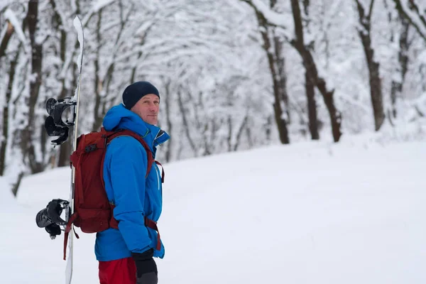 Aventureiro com snowboard e mochila fica na floresta — Fotografia de Stock