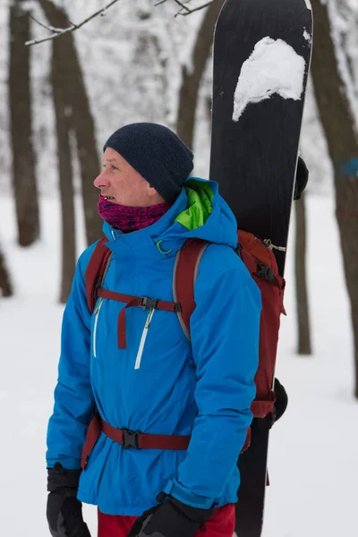 Счастливый сноубордист с рюкзаком стоит в лесу — стоковое фото