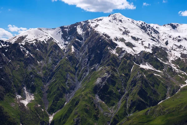 Rotsachtige bergketen met besneeuwde bergtoppen en groene hellingen — Stockfoto