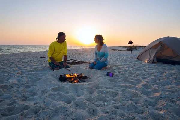 Happy adventurers sit next to burning bonfire on the beach
