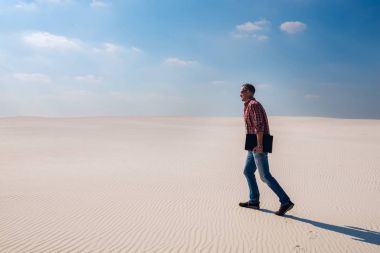 Neşeli Gezgin, adamın elinde dizüstü bilgisayar ile çöl boyunca girer