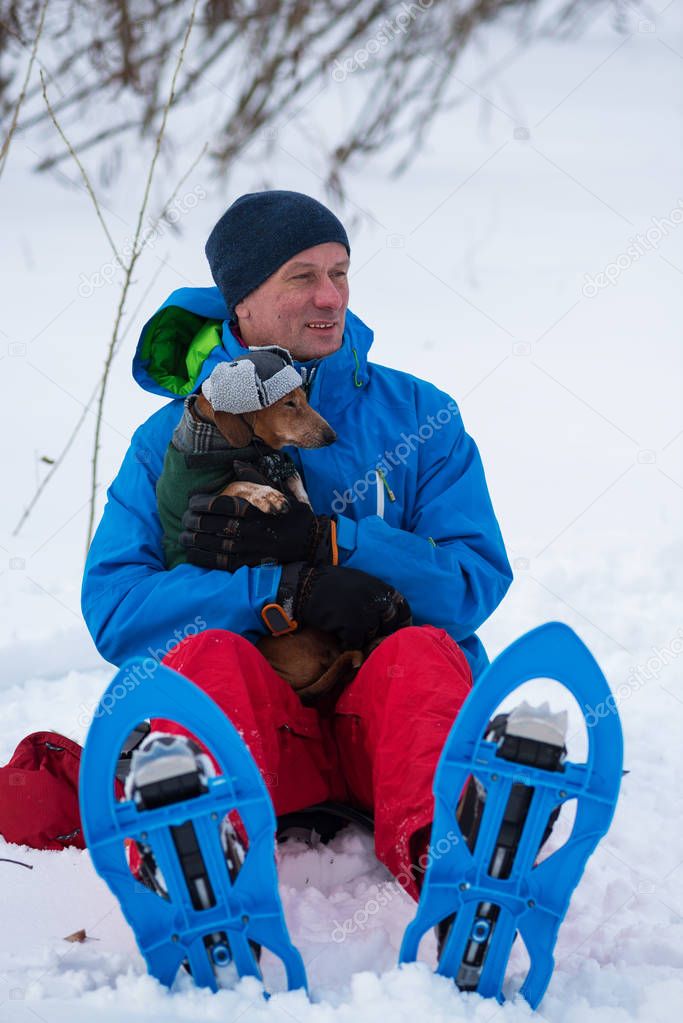 Happy traveler in snowshoes hugging a funny small dog 
