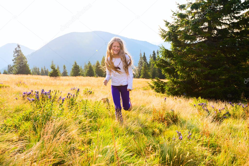 Happy teenage girl runs along the alpine meadow 