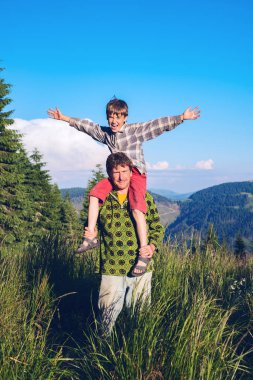 Gülümseyen baba neşeli küçük oğlu onun omuzlarında taşır.