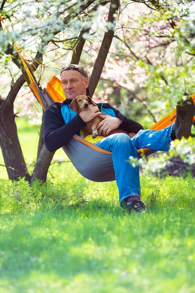 Dreaming man with his funny dog dachshund relaxes in a hammock