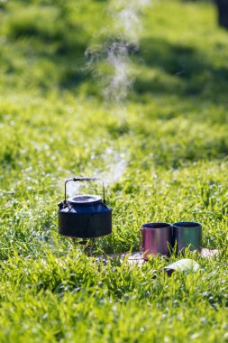 Küçük çelik su ısıtıcısı gaz brülör yanındaki iki çelik kupa üzerinde kaynatın olduğunu