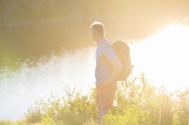 Sırt çantası ile yetişkin adam nehir kıyısında duruyor