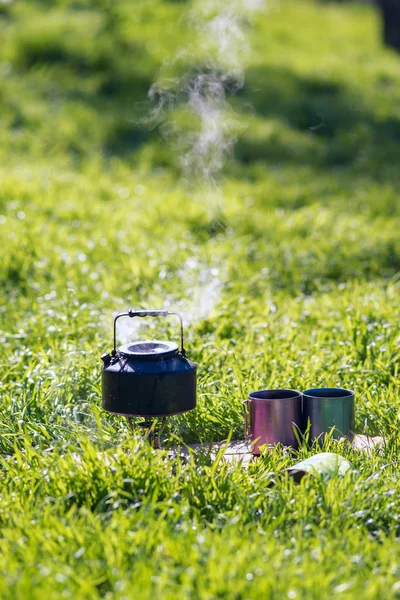 Küçük çelik su ısıtıcısı gaz brülör yanındaki iki çelik kupa üzerinde kaynatın olduğunu