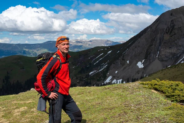 Aventurero sonriente con mochila se levanta en un prado de montaña verde — Foto de Stock