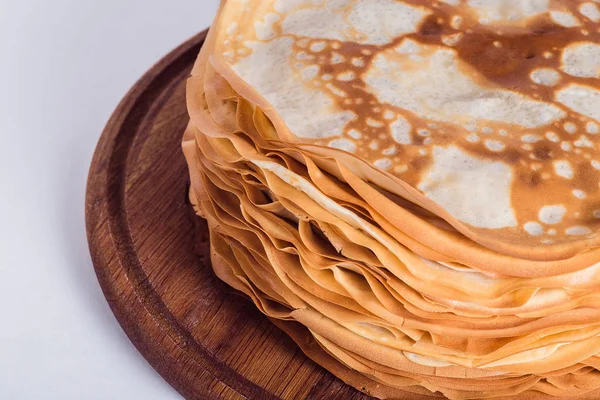 Thin pancakes on a round wooden stand on a white background — Stock Photo, Image