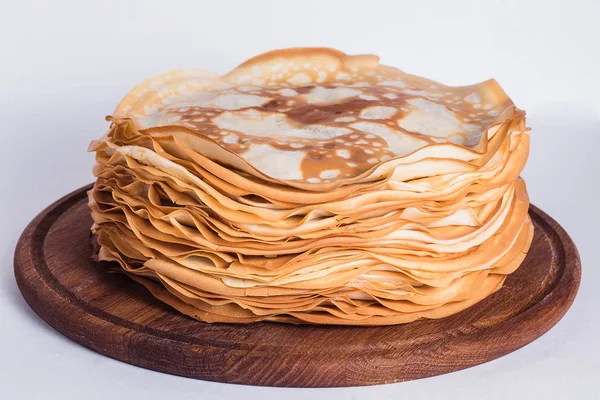 Thin pancakes on a round wooden stand on a white background — Stock Photo, Image