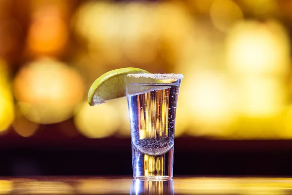 Un tequila de plata en un vaso sobre un fondo de luces brillantes . — Foto de Stock