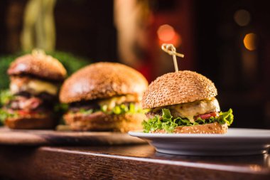 Karanlık bir arka plan üzerinde beyaz tabakta üç sulu lezzetli burger