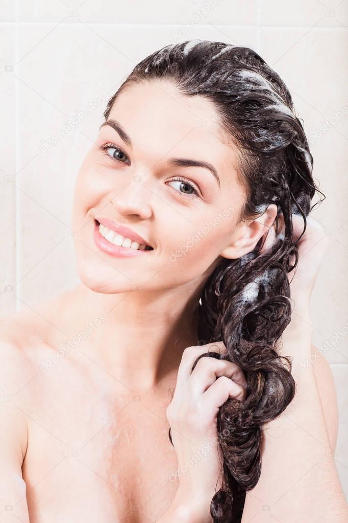 Young woman washing hair with shampoo in the shower