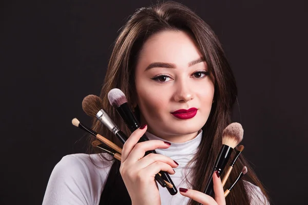 Make-up kunstenaar met penselen in de hand op een zwarte achtergrond — Stockfoto