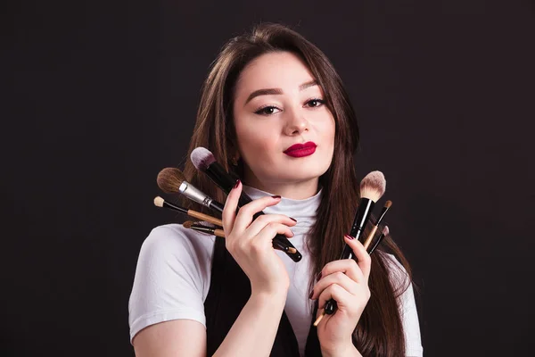 Make-up kunstenaar met penselen in de hand op een zwarte achtergrond — Stockfoto