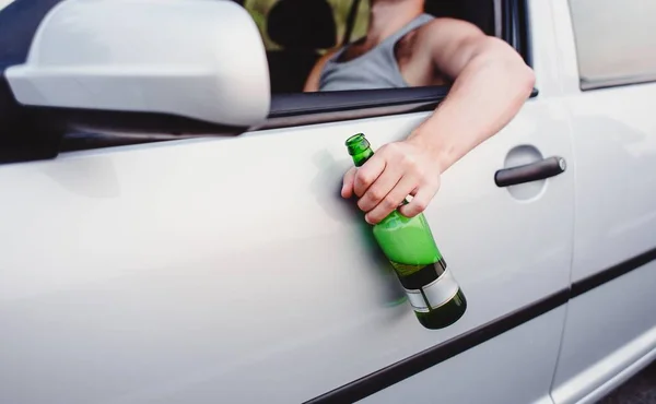 A drunk driver at the wheel of his car holds a bottle of beer in his hands.