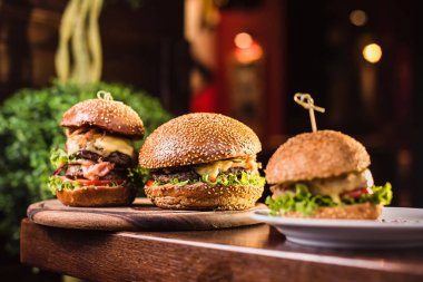Karanlık bir arka plan üzerinde beyaz tabakta üç sulu lezzetli burger