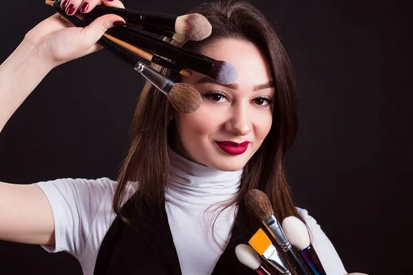 Make-up kunstenaar met penselen in de hand op een zwarte achtergrond — Stockfoto