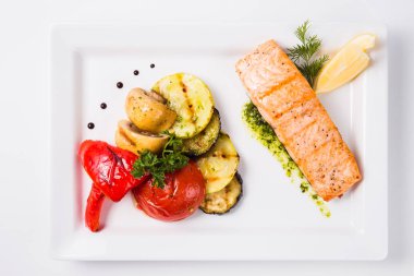 Sağlıklı gıda, kırmızı balık, sebze, otlar, limon üzerinde beyaz bir plat