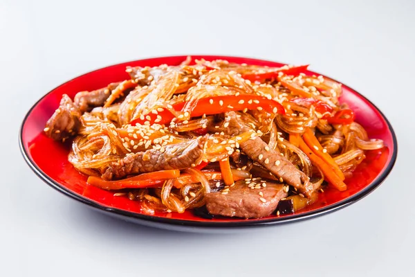 Noodles with  beef, pepper and sesame seeds on a red plate on a white background. Traditional Italian pasta. Close