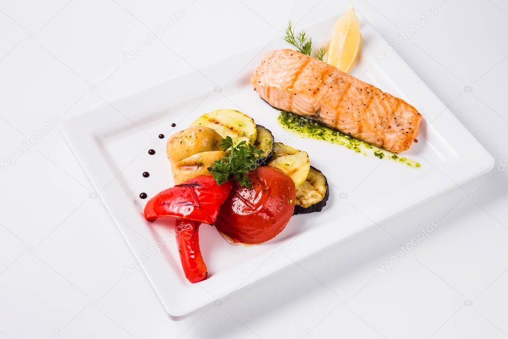 Healthy food, red fish, vegetables, herbs, lemon on a white plat